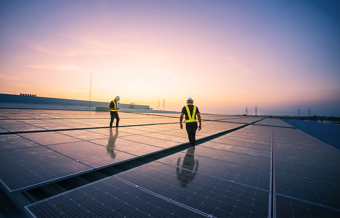 Two construction workers on an industrial building walking between solar cell panels on the roof of factory in the morning